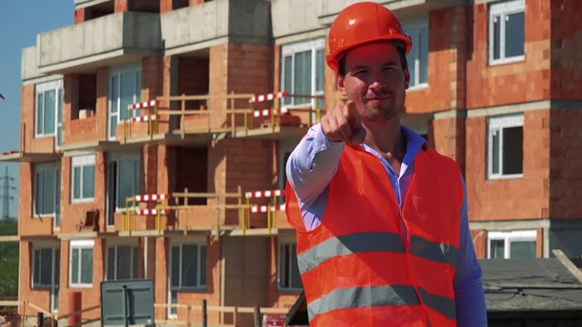 Construction worker points to the camera and agrees in front of building site