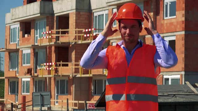 Construction worker puts the helmet on his head and smiles to the camera in front of building site 