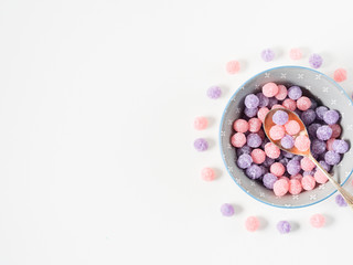 Round purple and pink bonbon candies sweets in gray bowl on white canvas background. Minimal still life