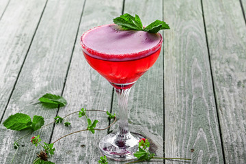 Classic frozen alcoholic cold drink with ice, raspberry, mint, martini and vodka in a glass. Cocktail with alcohol and fruit juice on a wooden table.