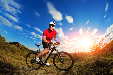 Fototapeta na wymiar Biker tourist travel on mountain bike. Autumn landscape. Sportsman on bicycle in red jersey and white helmet