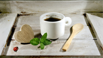 Coffee cup on wooden table with wooden heart mint leaves and a ladybug