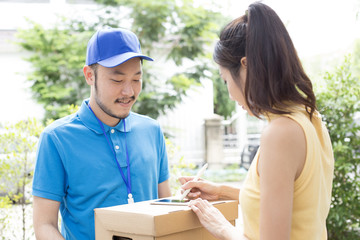 Young Asian Woman receive Box from  Delivery Man and Sign on Smartphone. People with Delivery Concept.