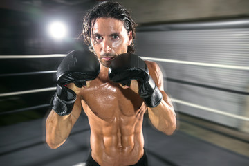 Tough muscular fighter with chiseled body stands in boxing ring ready to fight in attack stance