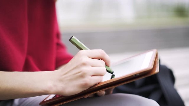 Close up of hands of an unrecognizable young woman wearing a red sweater working at her tablet computer with a special pen. Locked down real time close up shot