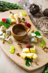 Close-up of a cheese plate. 4 types of cheese, soft white brie cheese, camembert, semi-soft briques, blue, roquefort, hard cheese. Walnuts, green grapes, sauce, white wine. Beautiful serve, restaurant