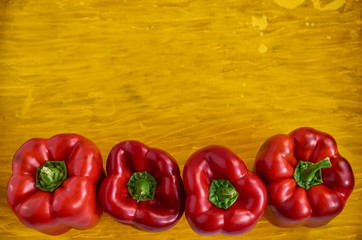 Four red bell peppers close up on wooden yellow background with copy space. Bell peppers on wooden yellow texture close up. Top view