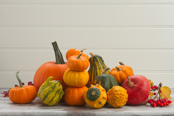 pile of orange pumpkins harvest with fall leaves and berries on white wooden table