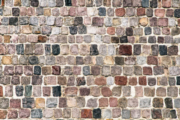 Old medieval restored stonewall texture background. Stone blocks are primarily of reddish and blue color.