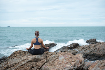 Young asian woman yoga and meditation on the stone at the sea beach, healthy lifestyle and fitness concept.