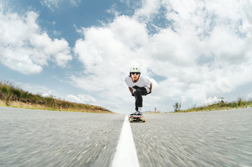 A guy wearing a helmet and sunglasses is riding his longboard on a country road