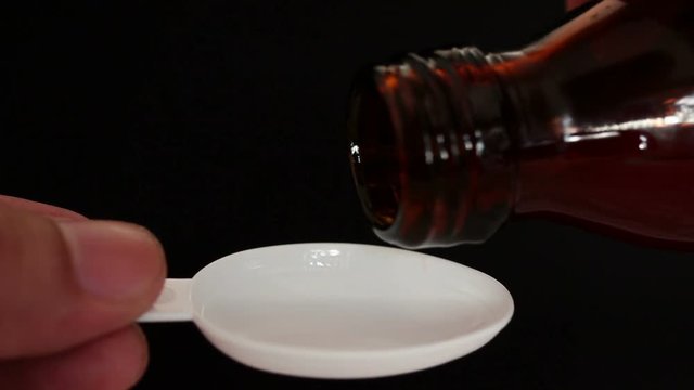 Liquid medicine pouring from a bottle on a teaspoon.
