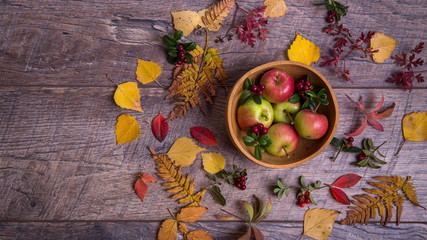 Autumn arrangement of leaves, apples and berries on a wooden background with free space for text. Top view, concept of the season
