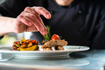 Chef finishing and garnishing food he prepared, a dish with pork meat and vegetables - obrazy, fototapety, plakaty