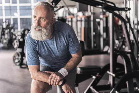 Melancholy senior male is standing in modern gym