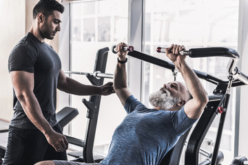 Concentrated old male is having workout with his trainer