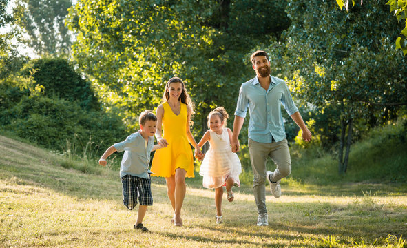 Active young parents with a healthy lifestyle running together with their two competitive children outdoors in a summer day