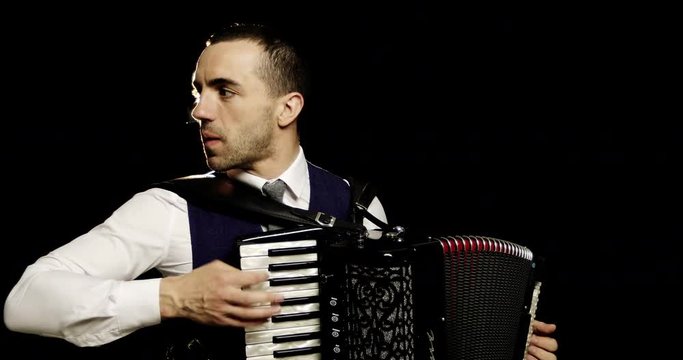 A fashionable musician in a white shirt plays the accordion in the studio on a black background.