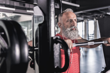 Pensive serious male with beard enjoying workout in athletic center