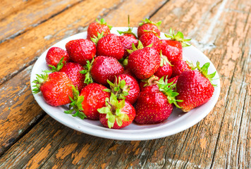 Fresh red strawberries in a white bowl standing on the rustic wooden table