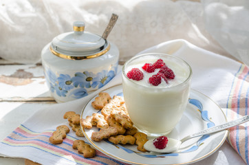 Milk yogurt with raspberries in a transparent glass is on the windowsill