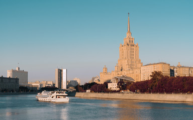 Obraz premium Autumn cityscape on sunny evening: Moscow river with touristic ship on it, historical hotel building calling 