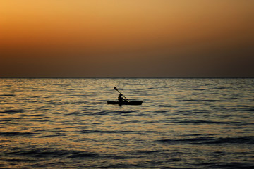 Fototapeta premium Young man floating on the canoe in the sea at sunset