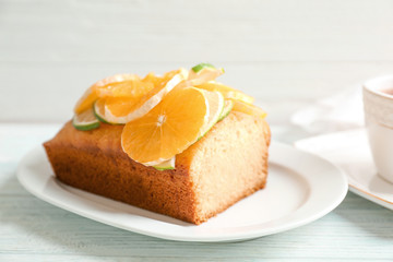 Plate with delicious sliced citrus cake and orange on wooden table