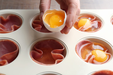 Woman adding egg into muffin tin with ham, closeup