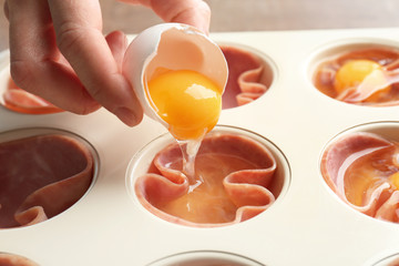 Woman adding egg into muffin tin with ham, closeup
