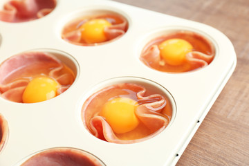 Muffin tin with raw eggs and ham, closeup