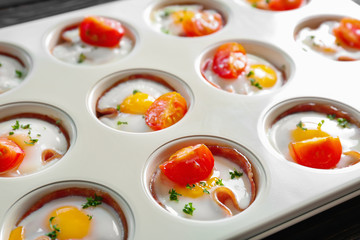 Baking mold with tasty eggs, tomatoes and ham on table, closeup