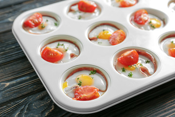 Muffin tin with tasty eggs, tomatoes and ham on table