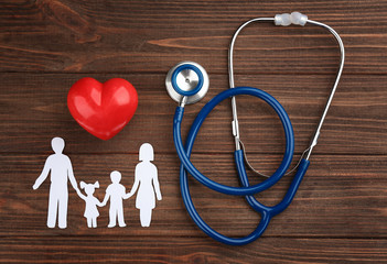 Paper silhouette of family, stethoscope and heart on wooden background. Health insurance concept
