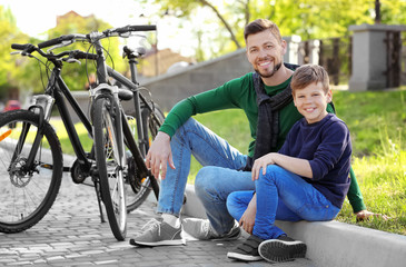 Dad and son sitting with their bicycles outdoors