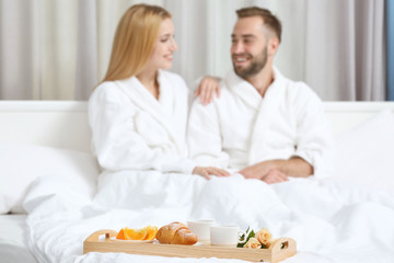 Tray with breakfast in hotel room and happy young couple on background