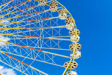 A Ferris wheel and its colorful passenger baskets against blue sky.