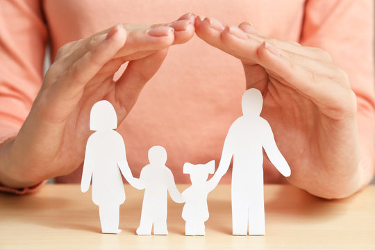 Woman covering paper silhouette of family with hands, closeup. Insurance concept
