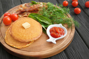 Tasty breakfast with pancakes, bacon and vegetables on wooden board