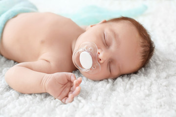 Cute little baby with pacifier sleeping on soft plaid