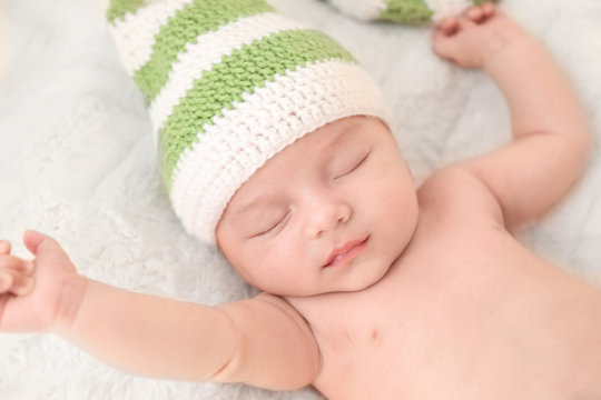 Cute little baby in knitted cap sleeping on bed at home