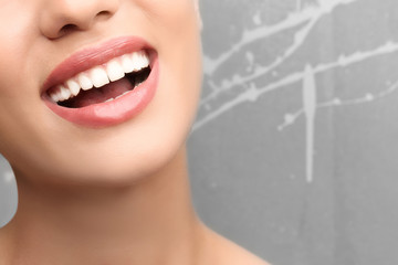 Young woman with healthy teeth laughing on grey background, closeup
