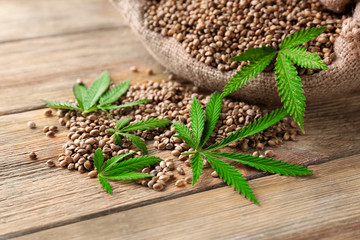Heap of hemp seeds in bag on wooden background