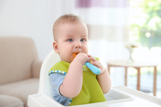 Cute baby with spoon sitting in kitchen