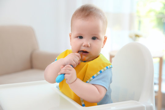 Cute baby with spoon sitting in kitchen