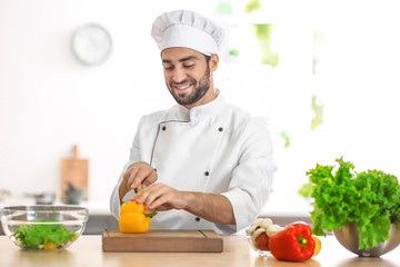 Young male chef cutting paprika in kitchen