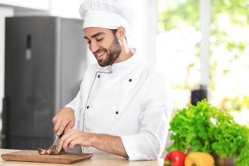 Young male chef cutting meat in kitchen