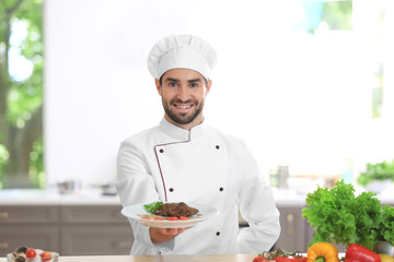 Young male chef holding freshly cooked dish in kitchen