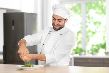 Young male chef adding spices to salad in kitchen
