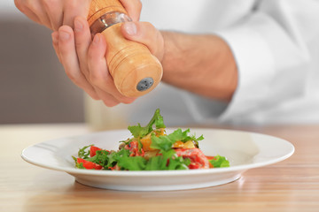 Male chef adding spices to salad in kitchen, closeup